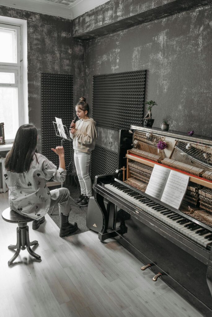 A music teacher guides a girl in an indoor piano lesson.