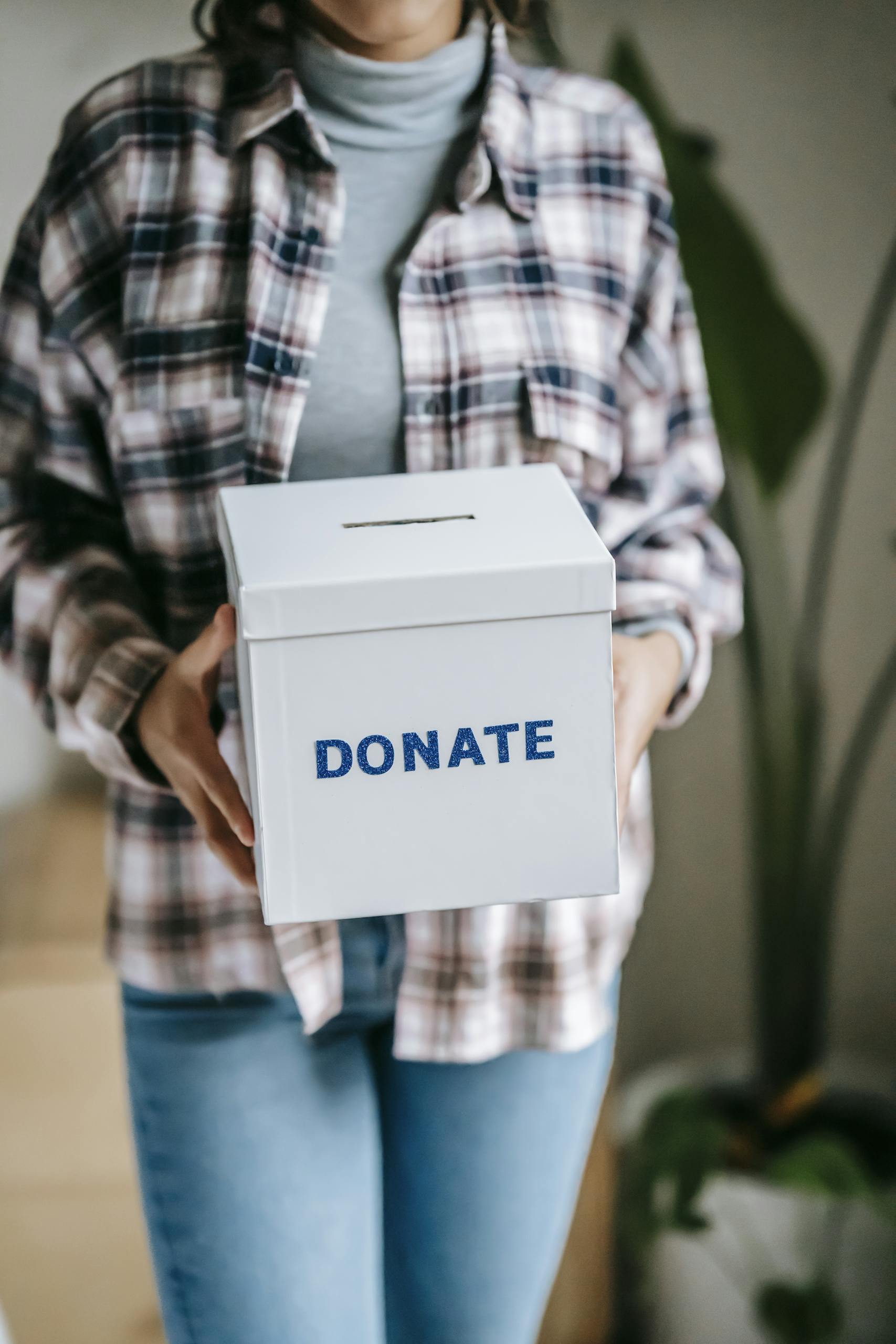 Crop unrecognizable woman in casual clothes standing with box for donations in hands on light room